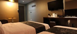 A hotel room with two beds, a desk with a computer, a television, and a coffee maker.