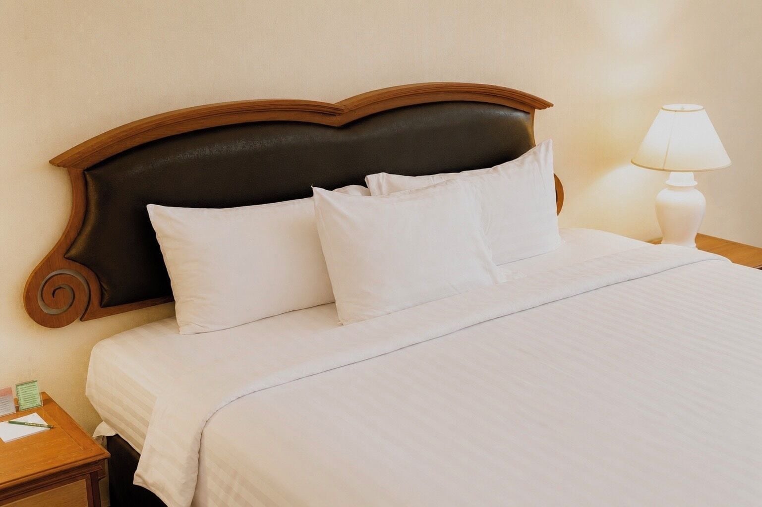A neatly made bed with white linens, a dark headboard, and a bedside table with a lamp.