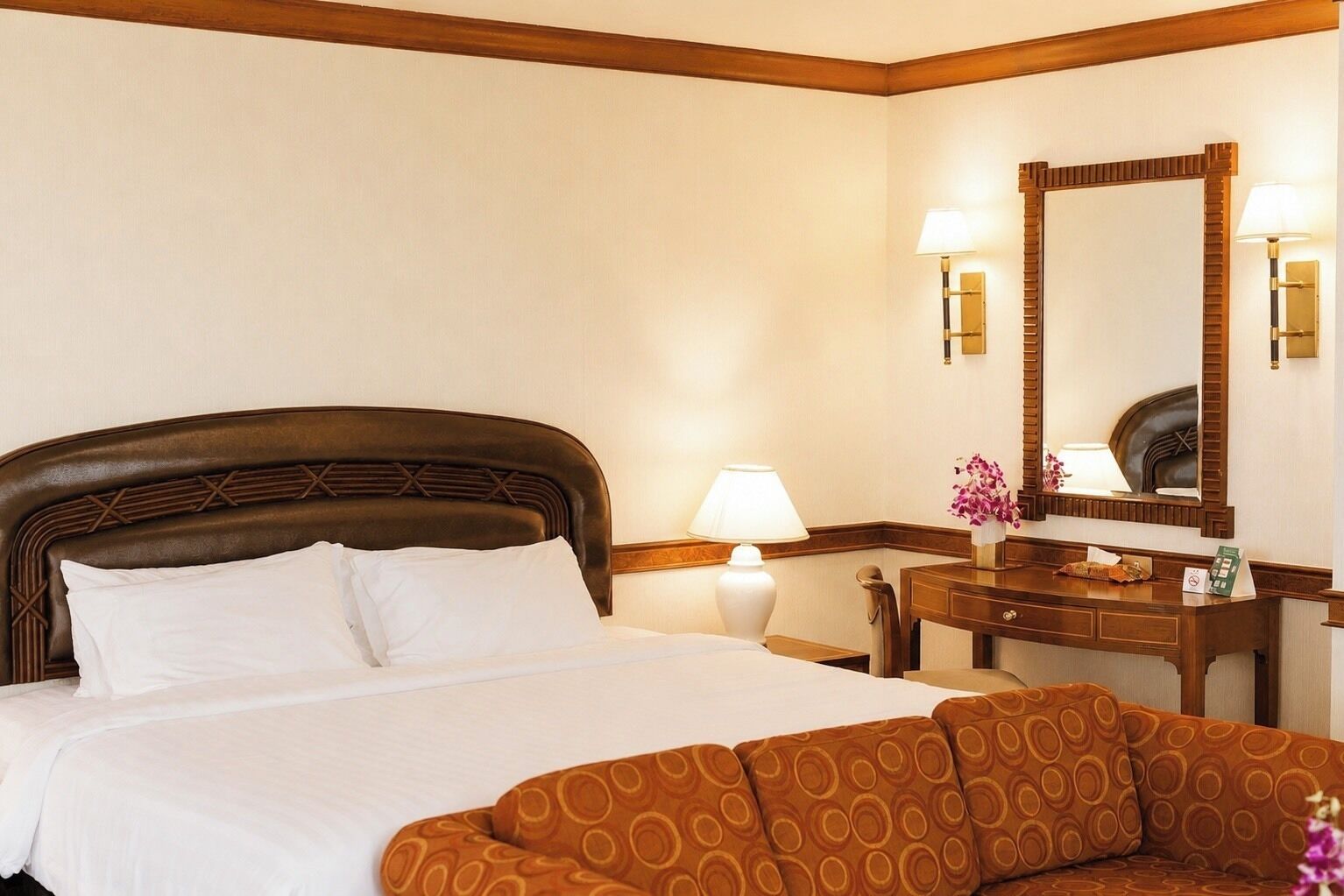 A hotel room with a bed, a sofa, a desk with a mirror, and a lamp.