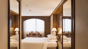 Ein Hotelzimmer mit einem großen Bett, zwei Nachttischen mit Lampen, einem Sofa und einem großen Bogenfenster.
