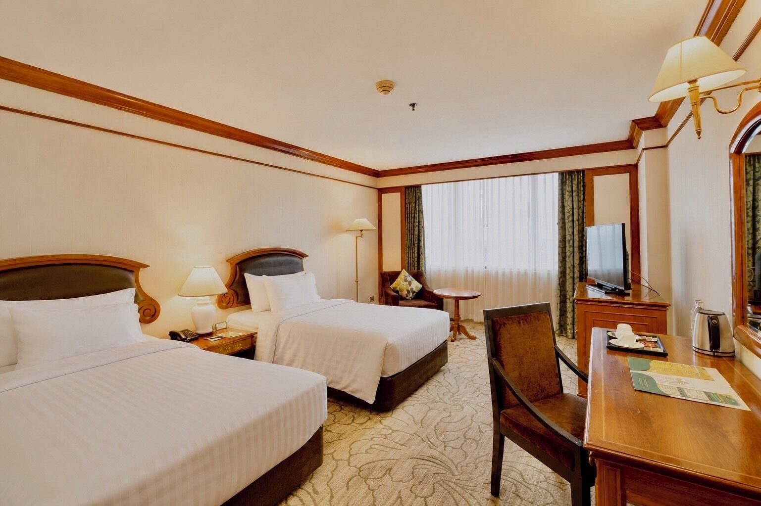 A hotel room with two beds, a desk, a chair, a television, and a window with curtains.