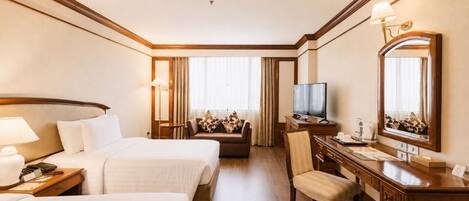 A hotel room with two beds, a sofa, a desk with a chair, a television, and a large mirror.