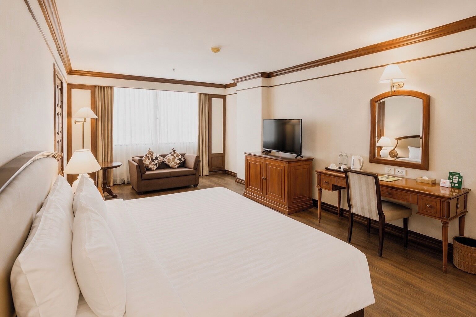 A hotel room with a large bed, a television, a desk with a chair, and a mirror.