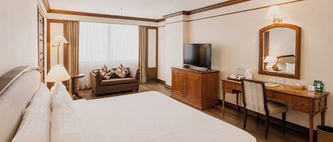 A hotel room with a large bed, a television, a desk with a chair, and a mirror.