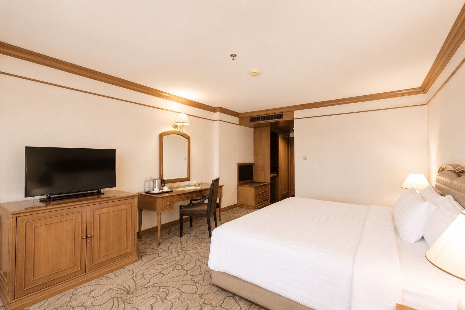 A hotel room with a bed, a desk with a TV, a mirror, and a wardrobe.