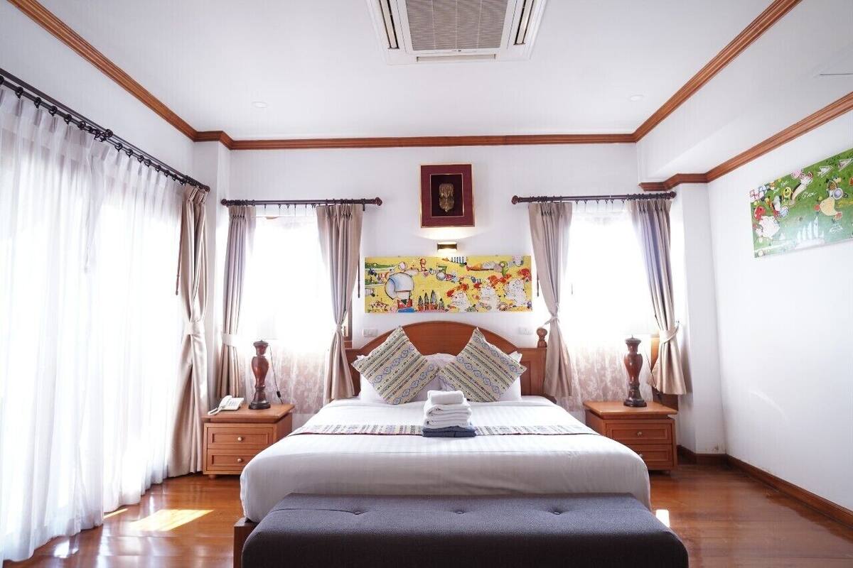 Une chambre d’hôtel avec un grand lit, deux tables de chevet, une petite table, une œuvre d’art accrochée au mur et une fenêtre avec des rideaux.
