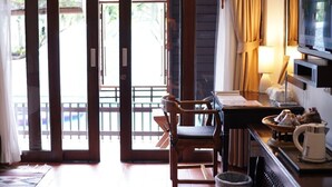 Une chambre d’hôtel avec un bureau en bois, une chaise, un téléviseur et une vue sur le balcon extérieur.
