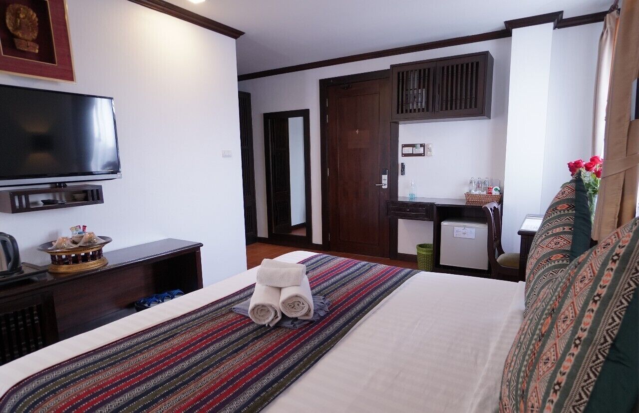 A hotel room with a bed, a TV, a desk, and a small kitchenette.