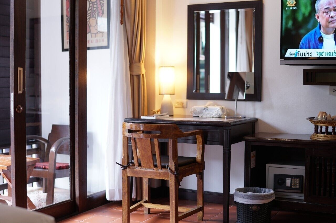 A hotel room with a wooden chair, a desk with a lamp, a television, and a small cabinet.