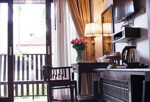 A hotel room with a wooden chair, a desk with a lamp, a television, and a window with curtains. - Baan Huen Phen (Chiang Mai)