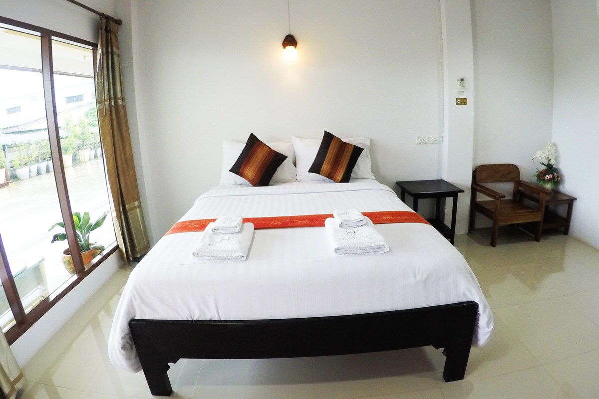 A hotel room with a large bed, two pillows, a nightstand, a chair, and a window with curtains.