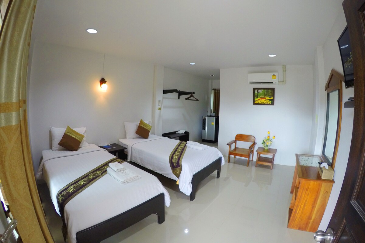 A hotel room with two beds, a desk, a chair, a mirror, and a small table with a vase.