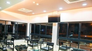 A modern indoor seating area with multiple tables and chairs, large windows, and a flat-screen TV mounted on the wall. - The Peak Boutique Hotel (Phra Phrom)