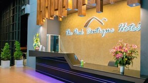 A reception desk with a modern design, a sign reading "The Peak Boutique Hotel", and potted plants on either side. - The Peak Boutique Hotel (Phra Phrom)