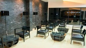 A modern interior with a stone wall, seating area with chairs and tables, and large windows. - The Peak Boutique Hotel (Phra Phrom)