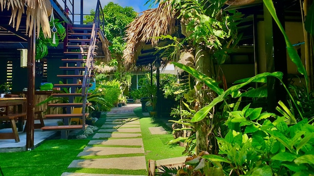 Uma trilha em um jardim tropical que leva a uma estrutura de madeira com telhado de palha.
