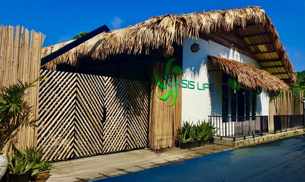 Un edificio con techo de paja, cerca de bambú y un letrero que dice "COAST LIME".