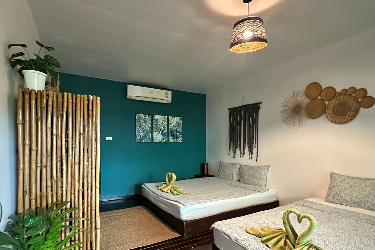 A modern bedroom with two beds, a bamboo wall, a hanging light fixture, and a wall-mounted air conditioner.