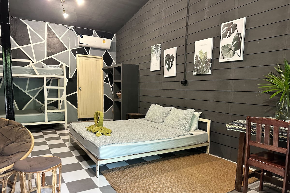 A bedroom with a bed, a chair, a small stool, a radiator, and wall art.