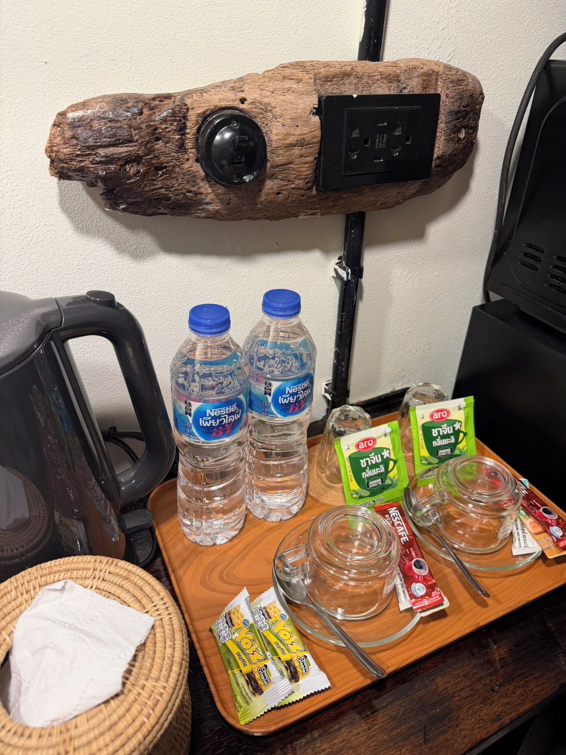 A kitchen counter with a rustic wooden shelf, two Nestlé water bottles, a tray with green tea packets, a glass mug, and a toaster.