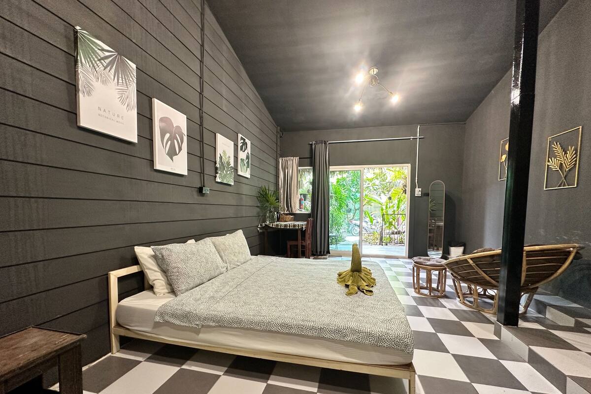 A modern bedroom with a large bed, a checkered floor, and framed botanical prints on the wall.