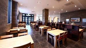 Un restaurante moderno con mesas y sillas de madera, un pilar de piedra y vistas de la ciudad a través de grandes ventanales.