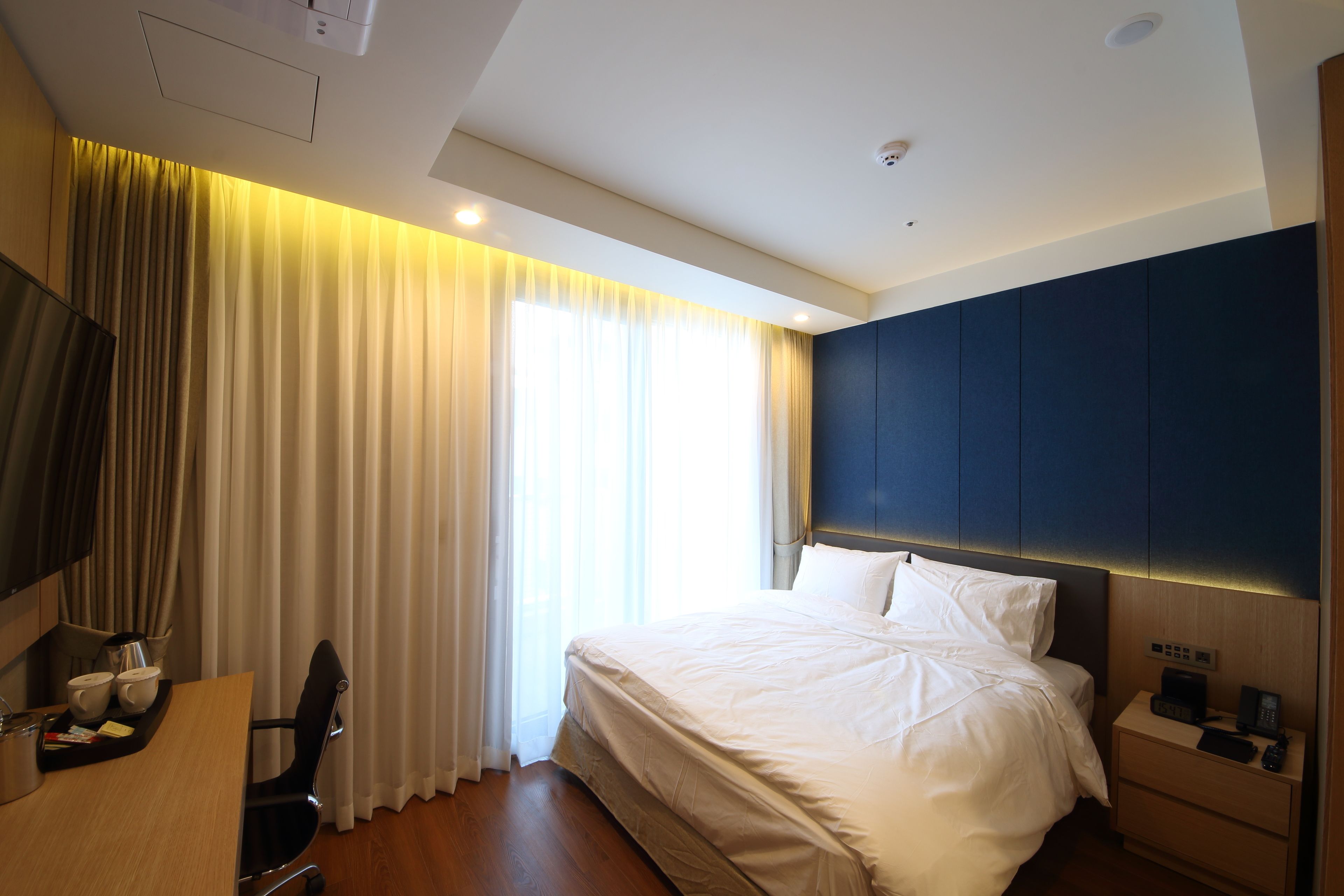 Een hotelkamer met een bed, nachtkastje, televisie en gordijnen.