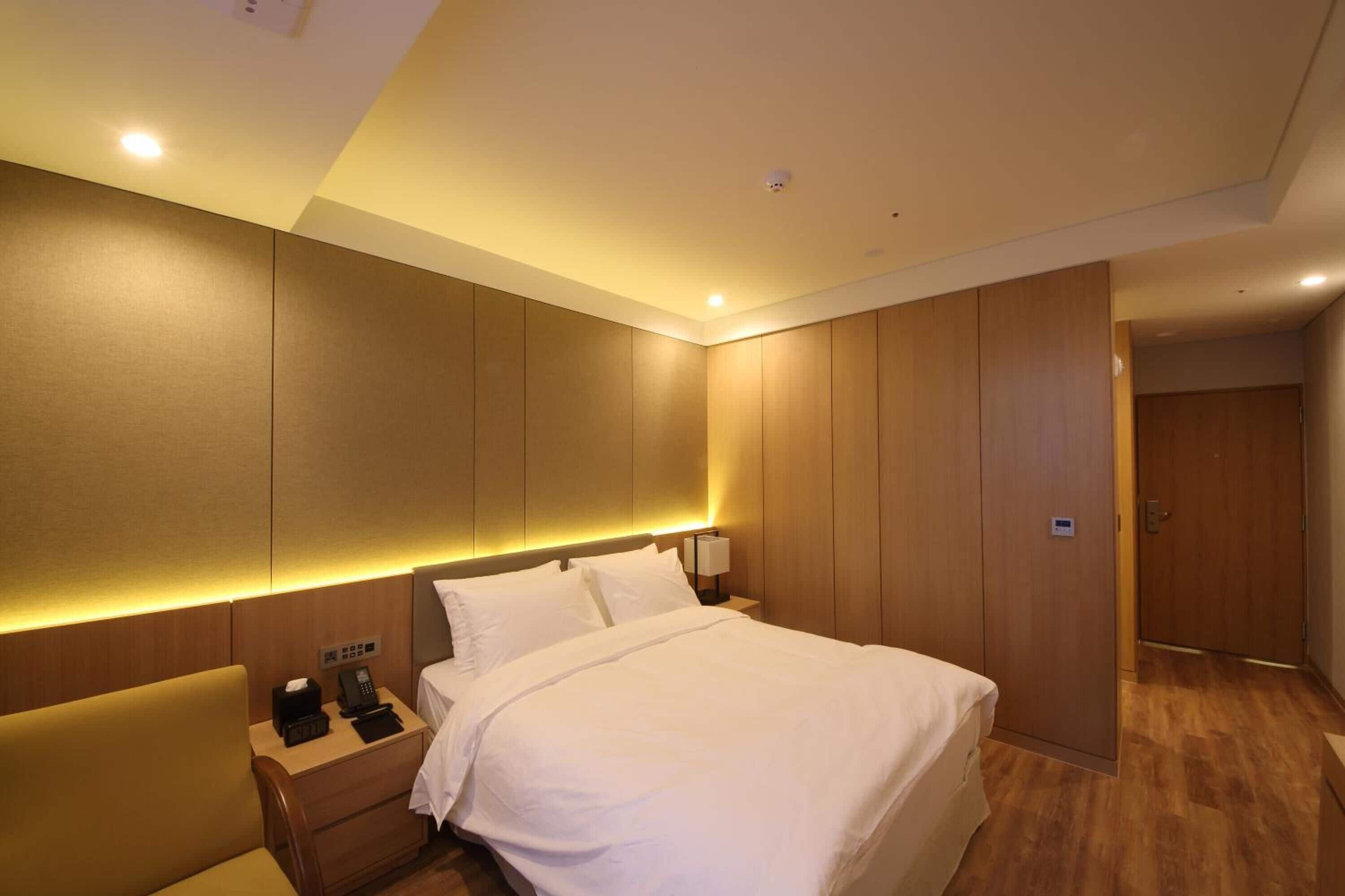 Ein Hotelzimmer mit einem großen Bett, einem Nachttisch mit Telefon und Lampe sowie einem Holzschrank.