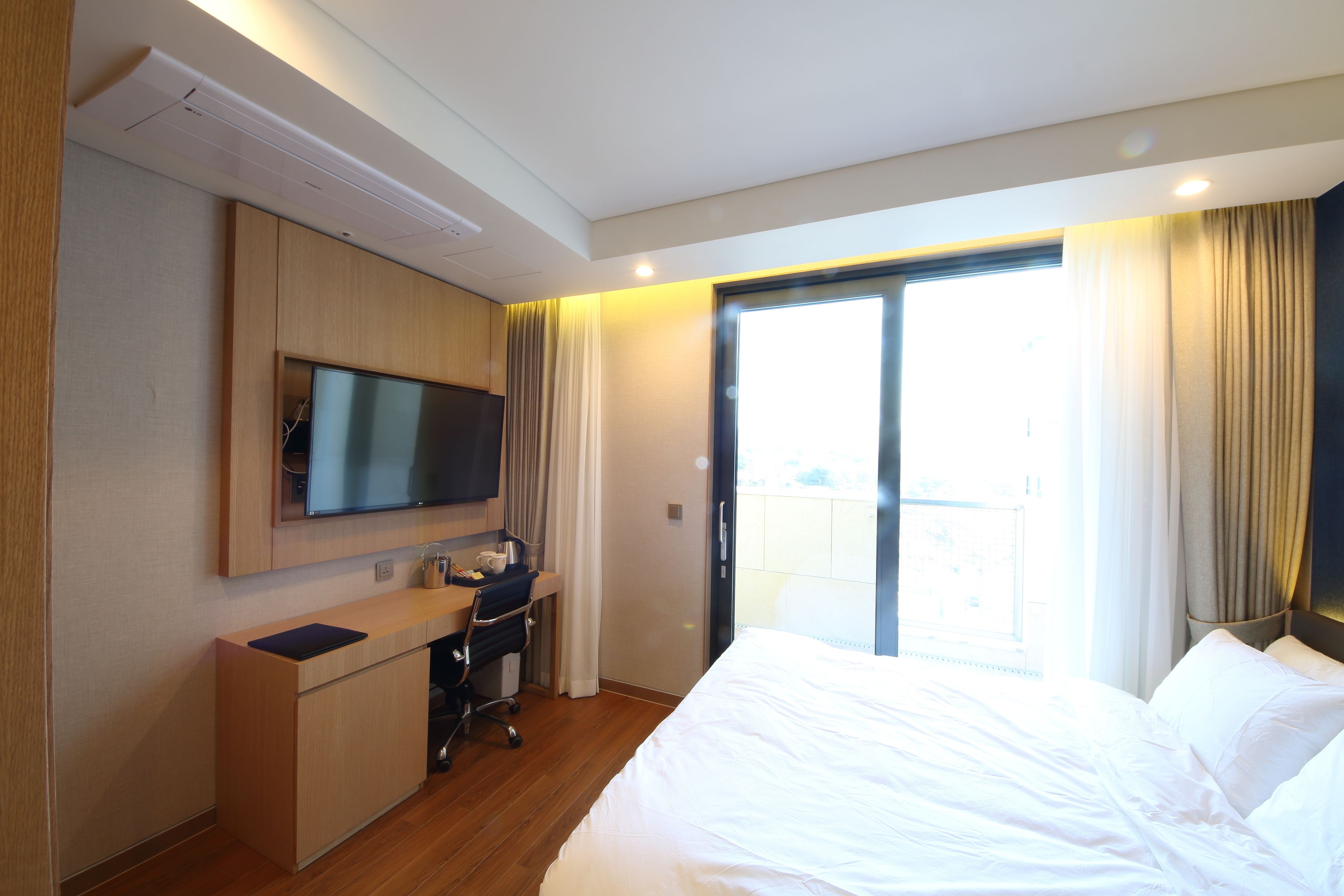 A hotel room with a bed, a desk, a television, and a sliding door to a balcony.