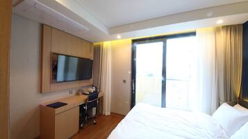A hotel room with a bed, a desk, a television, and a sliding door to a balcony.