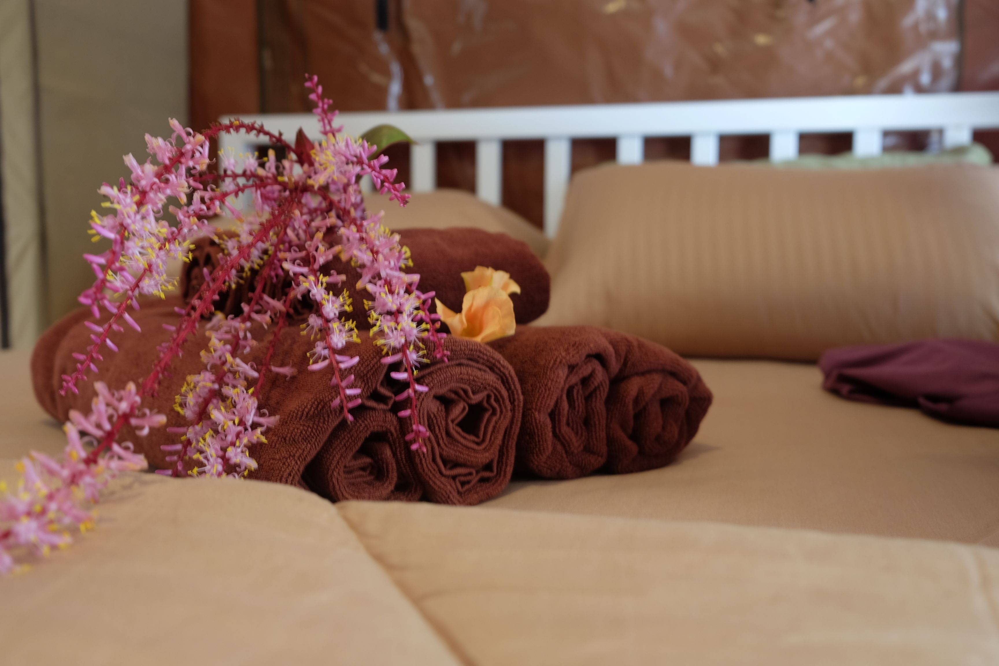 A neatly made bed with rolled towels and a decorative floral arrangement.