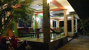 A covered outdoor area with a dining table and chairs, a hammock, and a motorcycle parked nearby. - Kama Siri (Ko Kood)