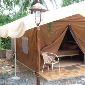 Una carpa con una cama en su interior, una silla y una lámpara en el exterior.