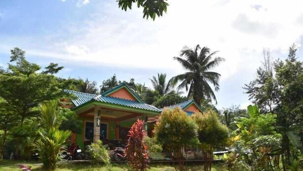 A house with a green roof and a porch, surrounded by lush greenery and palm trees. - Kama Siri (Ko Kood)