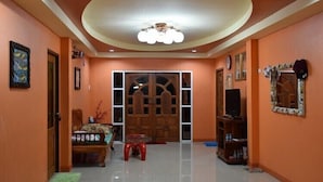 A spacious living area with a wooden door, a sofa, a small table, and a television. - Kama Siri (Ko Kood)