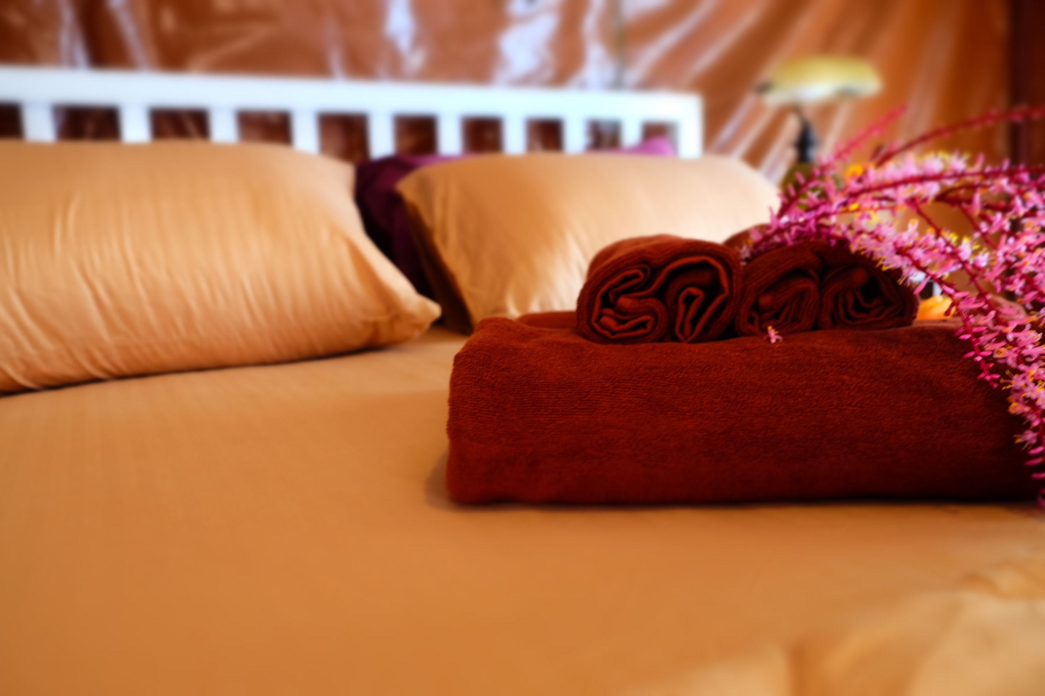 Een net opgemaakt bed met een rode handdoek en een opgerolde handdoek erop.