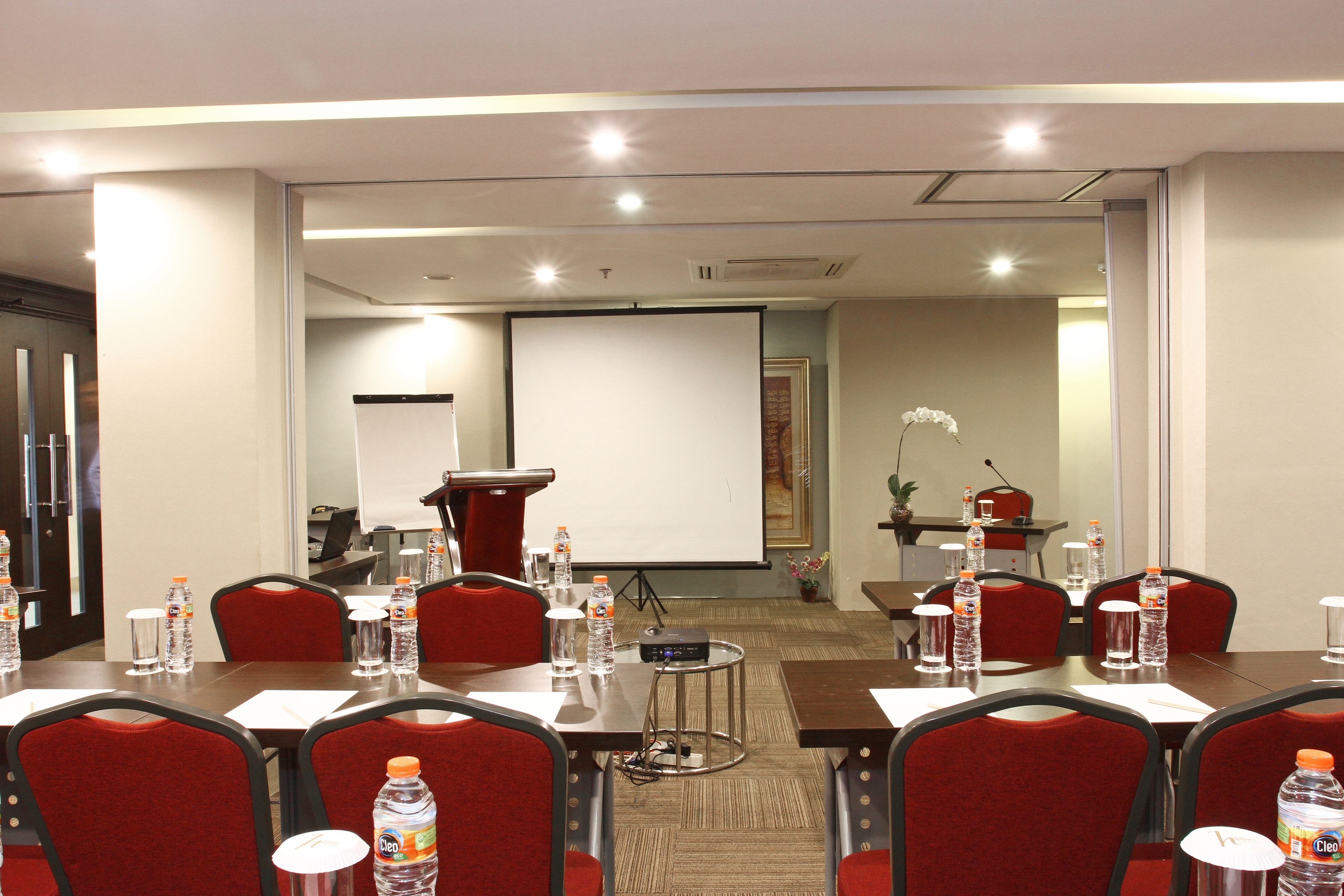 A conference room with tables, chairs, water bottles, a projector, and a presentation screen.