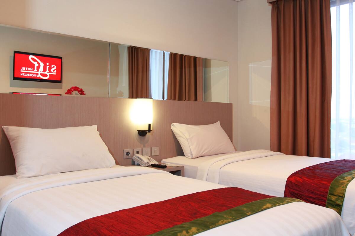 A hotel room with two beds, a wall-mounted TV, a phone, and a window with curtains.
