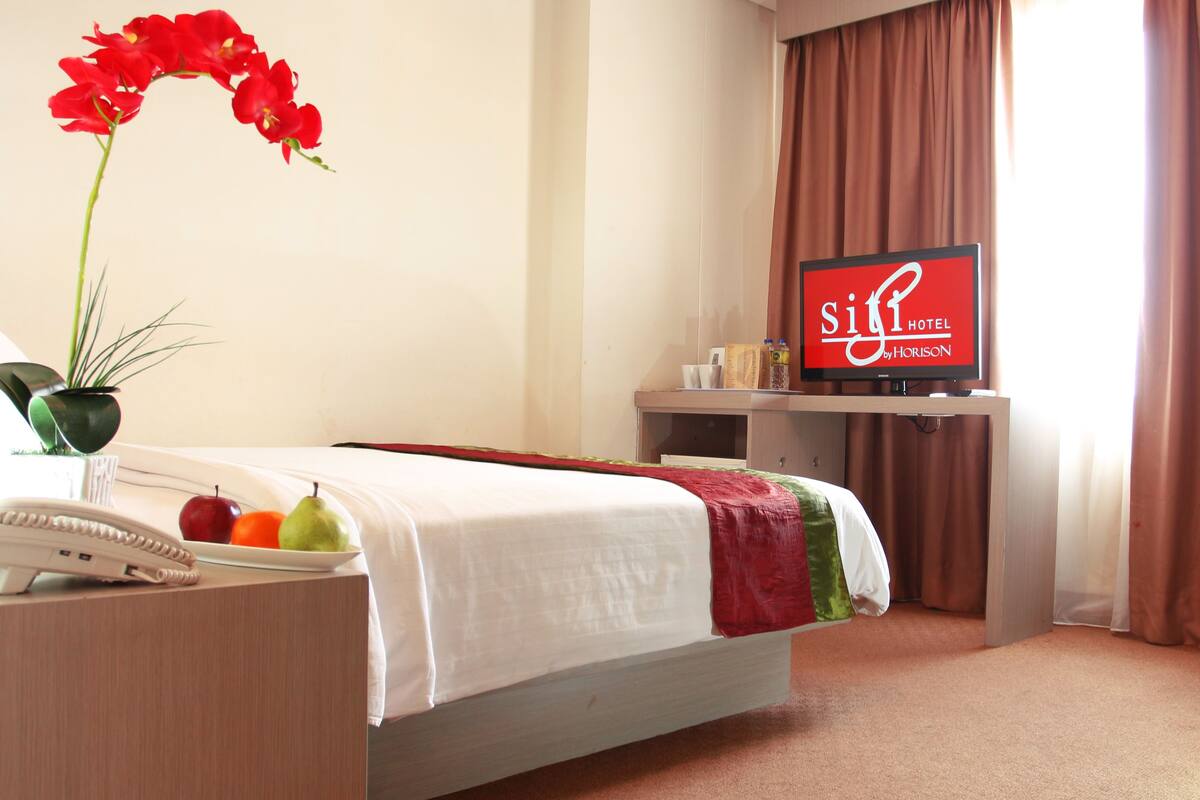 A hotel room with a bed, a desk with a telephone, a television, and a potted plant.
