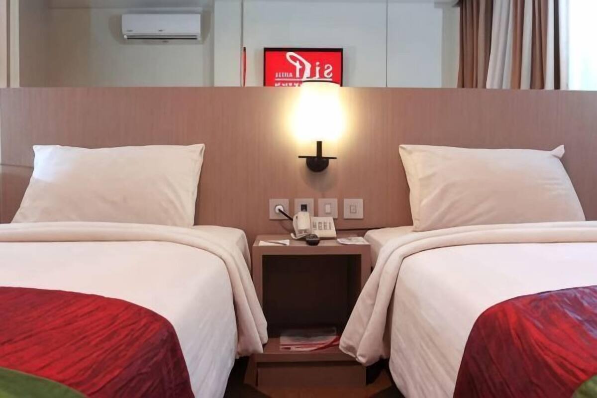 A hotel room with two beds, a nightstand with a lamp, and a sign above the beds.