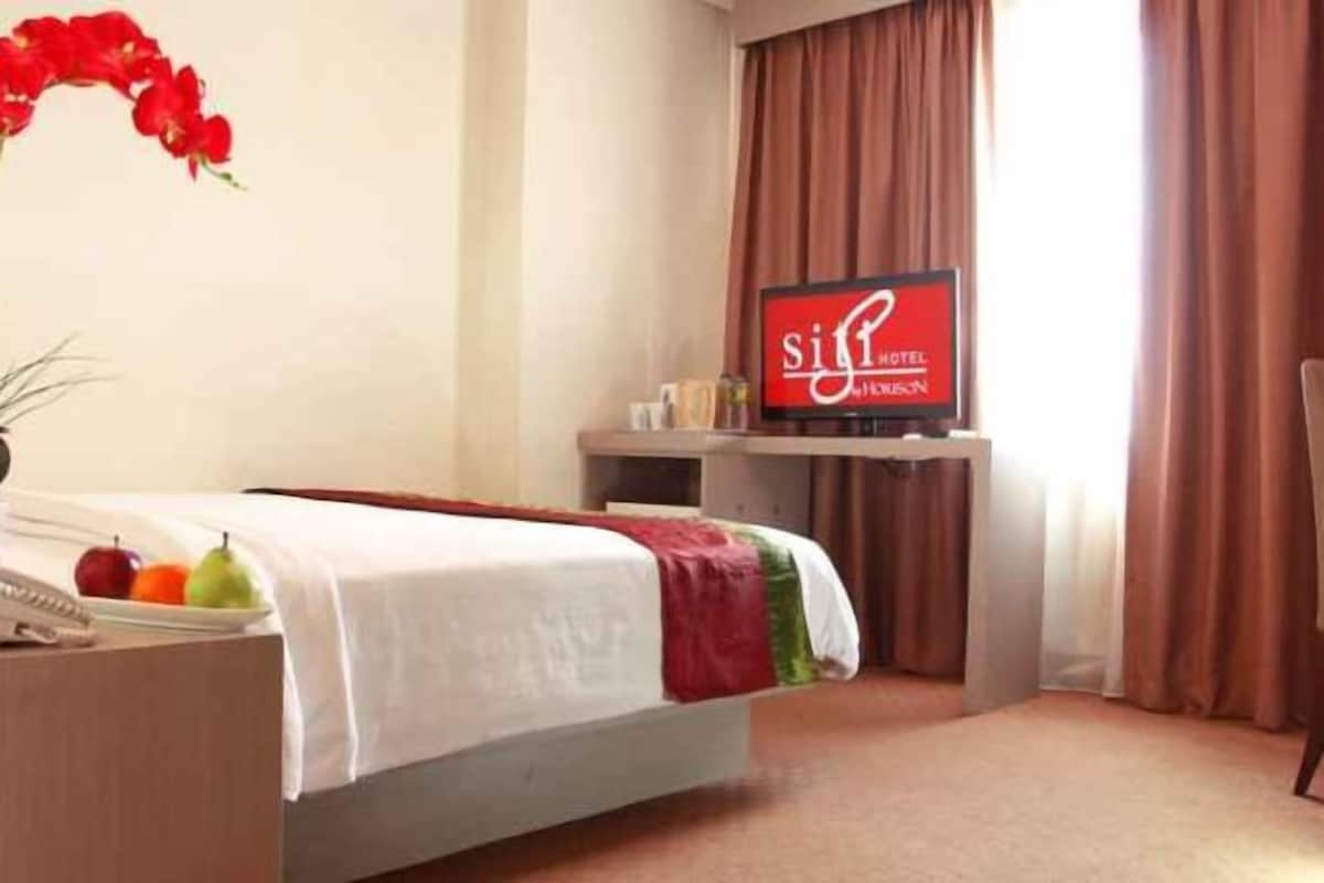 A hotel room with a bed, a TV, a desk with a phone, and a vase with flowers.