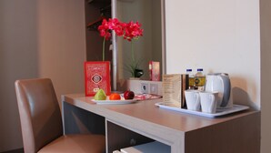 Escritorio de habitación de hotel con una bandeja de fruta, una orquídea roja, un menú y una tetera.