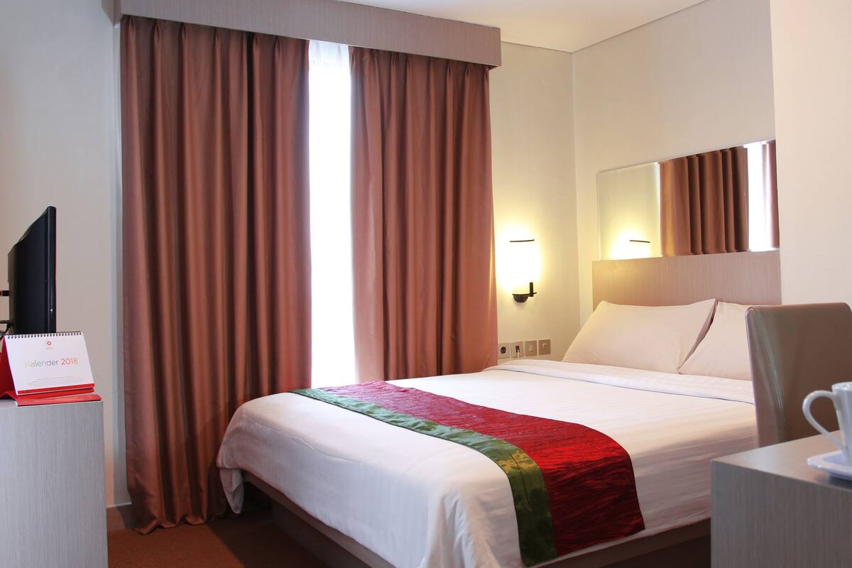 A hotel room with a bed, a desk with a coffee maker, a mirror, and a calendar on the wall.
