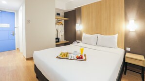 A hotel room with a neatly made bed, a tray with breakfast, a bedside table, and a wardrobe. - Hotel Citradream Bintaro (South Tangerang)