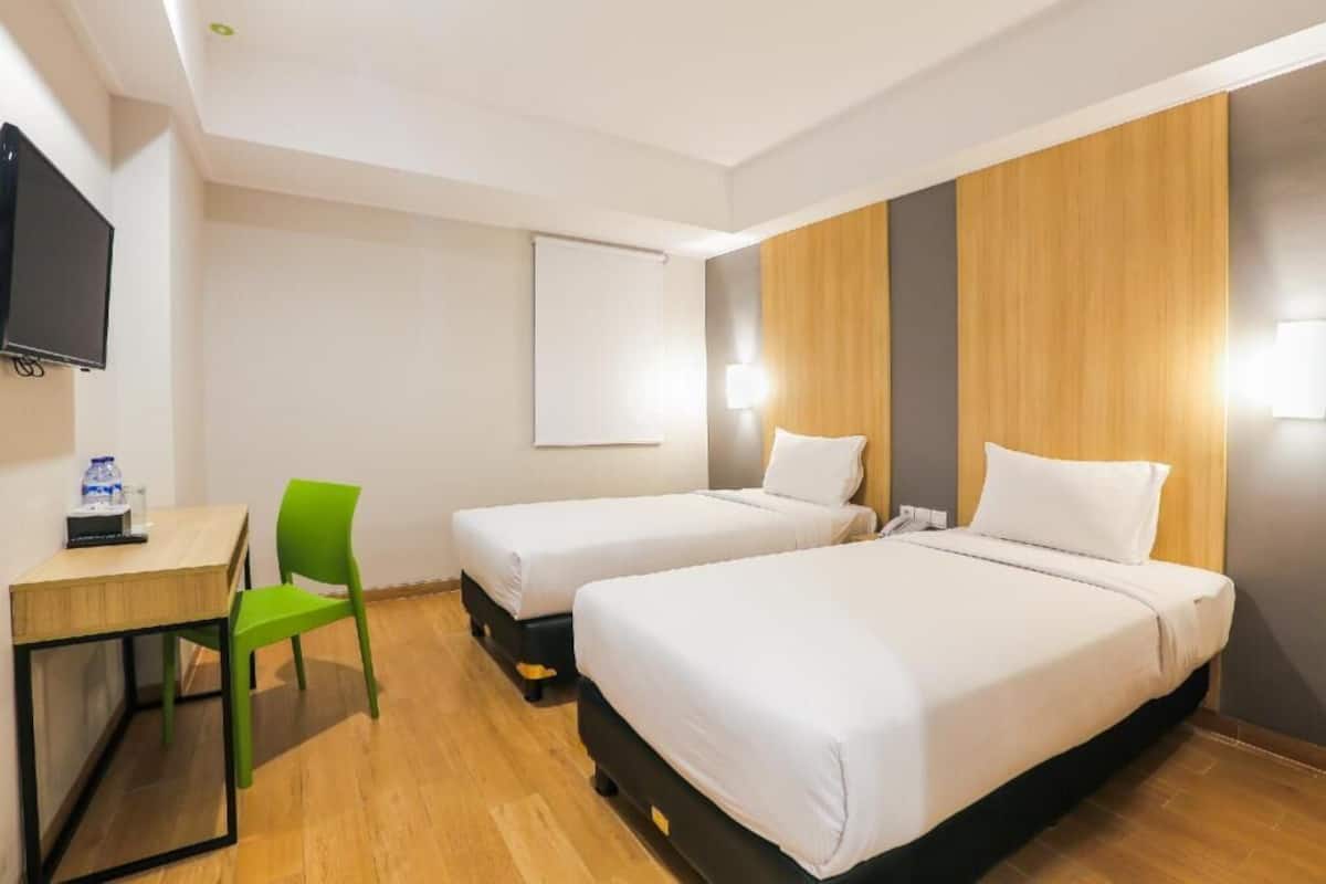 A hotel room with two beds, a desk, a chair, a TV, and a projector screen.