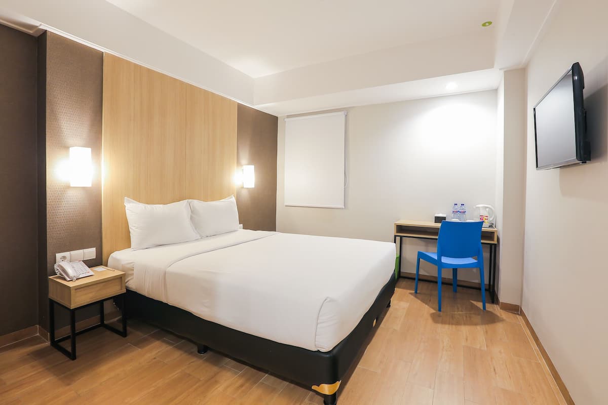 A hotel room with a bed, bedside table, desk, chair, and a flat-screen TV.