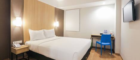 Habitación de hotel con cama, mesita de noche, escritorio, silla y televisor de pantalla plana.