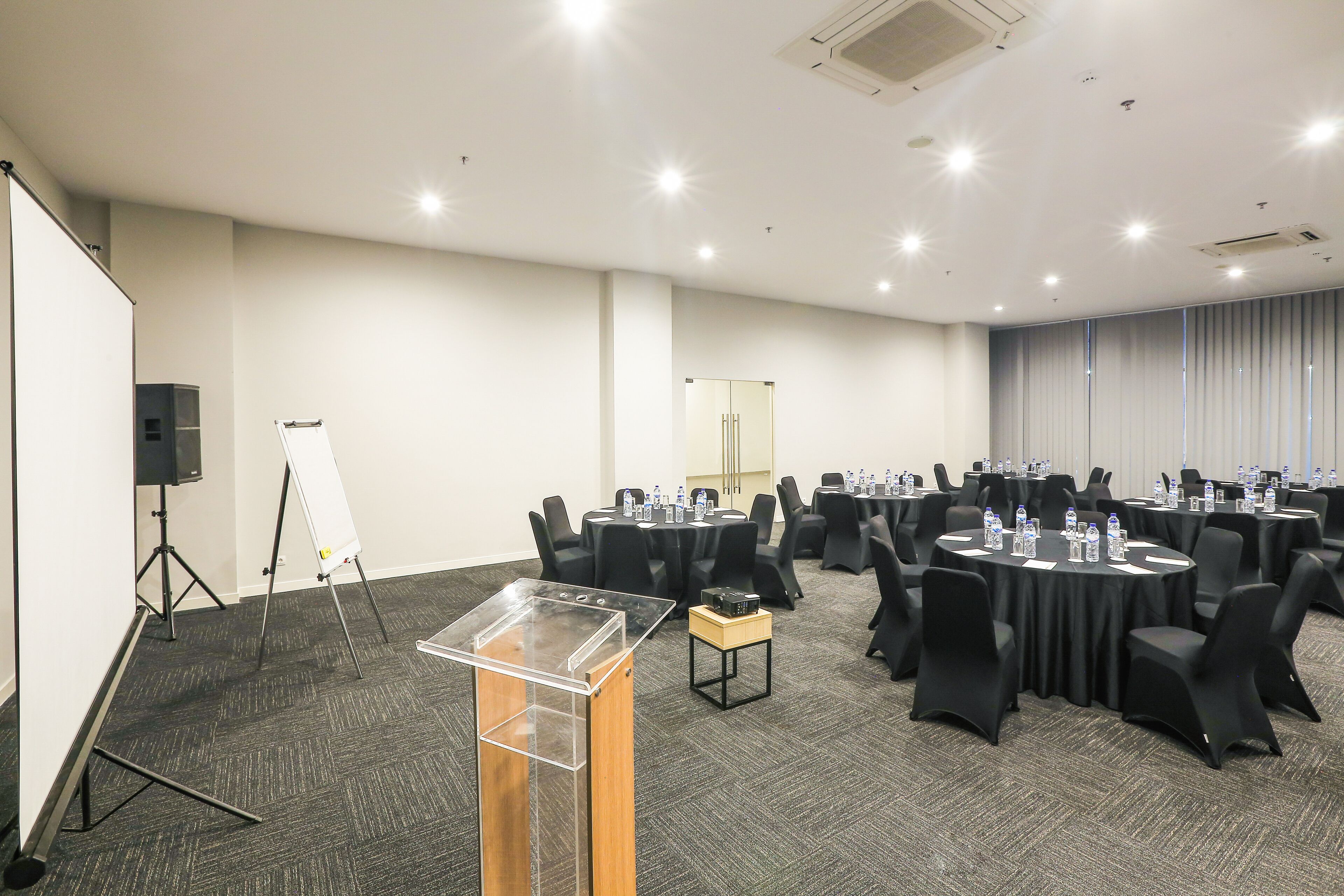 A conference room with round tables, black chairs, a podium, and a whiteboard.