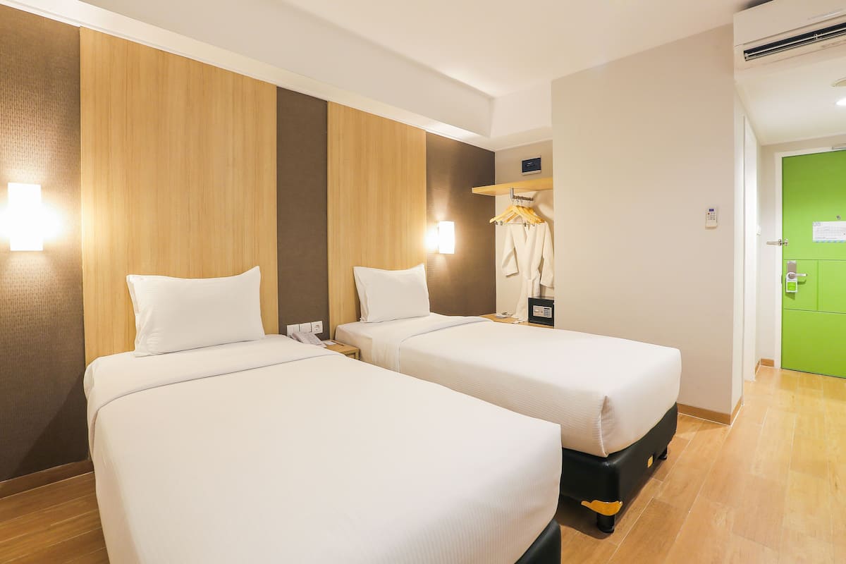 A hotel room with two beds, a wooden accent wall, a green door, and a coat hanging on a rack.