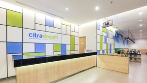 A hotel reception area with a modern design, featuring a wooden reception desk, a colorful wall with the hotel name, and a seating area with a coffee machine. - Hotel Citradream Bintaro (South Tangerang)